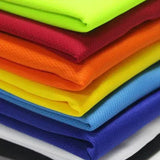 A stack of vibrant, folded fabrics showcasing colors: neon green, red, orange, yellow, light blue, dark blue, and white.