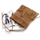A stylish brown suede handbag with fringe detailing and metallic studs, resting on a fashion magazine.