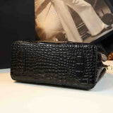 Sleek black crocodile-patterned handbag resting on a table with a blurred background of fashion imagery.
