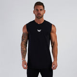 A muscular man stands confidently in a black sleeveless shirt with a small white logo, set against a plain gray background.