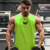 A muscular individual wearing a bright green sleeveless top holds a dumbbell in each hand while posing in a gym setting.