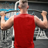 A muscular man in a red sleeveless shirt performs a pull-up in a gym, showcasing his strong back and arms.