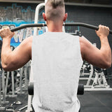A muscular man in a sleeveless shirt performs a pull-up in a gym, with exercise equipment and graffiti visible in the background.