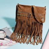 A stylish brown fringe handbag with studs and a zipper, resting on a light blue surface beside a beauty magazine and a mirror.