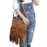 A woman in denim overalls holds a fringed brown suede handbag adorned with studs, showcasing a casual, stylish look.