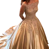 A woman in an elegant, gold off-shoulder ball gown with intricate lace details stands with her back turned, conveying a sense of grace and luxury.