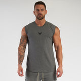 A muscular individual stands confidently wearing a sleeveless gray shirt and light gray shorts, showcasing his tattoos.