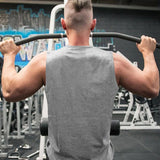 A muscular man wearing gray shirt with a short hairstyle performs a lat pull-down exercise at a gym, showcasing his toned back and arms.