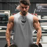 A muscular individual holds dumbbells, showcasing defined arms, wearing a gray sleeveless shirt with a logo. Gym setting in the background.