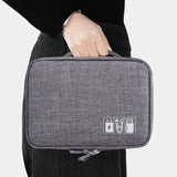 A person holding a gray tech organizer bag with icons for charging and USB cables on the front, against a plain background.