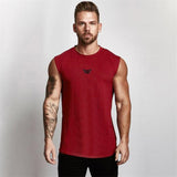 A muscular man in a red sleeveless shirt showcases arm tattoos against a plain background, emphasizing fitness and style.