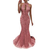 A woman wearing a shimmering, rose-pink sequin gown with a halter neck and open back. The dress has a fitted silhouette and a flowing train.