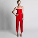 A woman in a fitted, strapless red jumpsuit poses confidently against a gray background