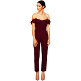 A woman in a maroon, off-shoulder jumpsuit with ruffles stands confidently against a white background, exuding elegance and sophistication.