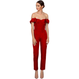 A woman in a red off-the-shoulder jumpsuit with ruffled sleeves stands against a white background. She exudes elegance, looking to the side.