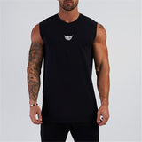 A muscular man wearing a sleeveless black top with a white winged logo, showcasing tattoos on his arms against a plain background.