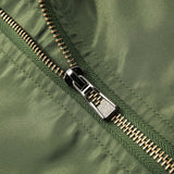 Close-up of a metal zipper on green fabric, showing detailed stitching and texture. The shiny silver zipper contrasts with the matte cloth surface.
